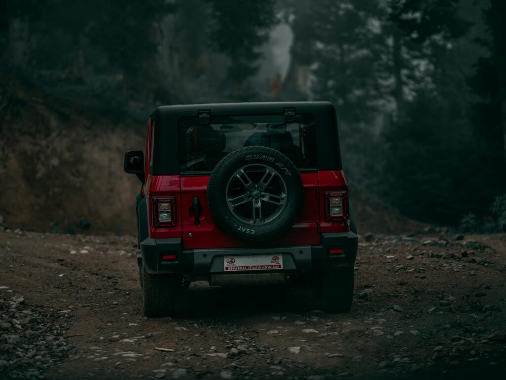 A red off-road vehicle travels down a rugged dirt path surrounded by forest scenery, perfect for adventure seekers.