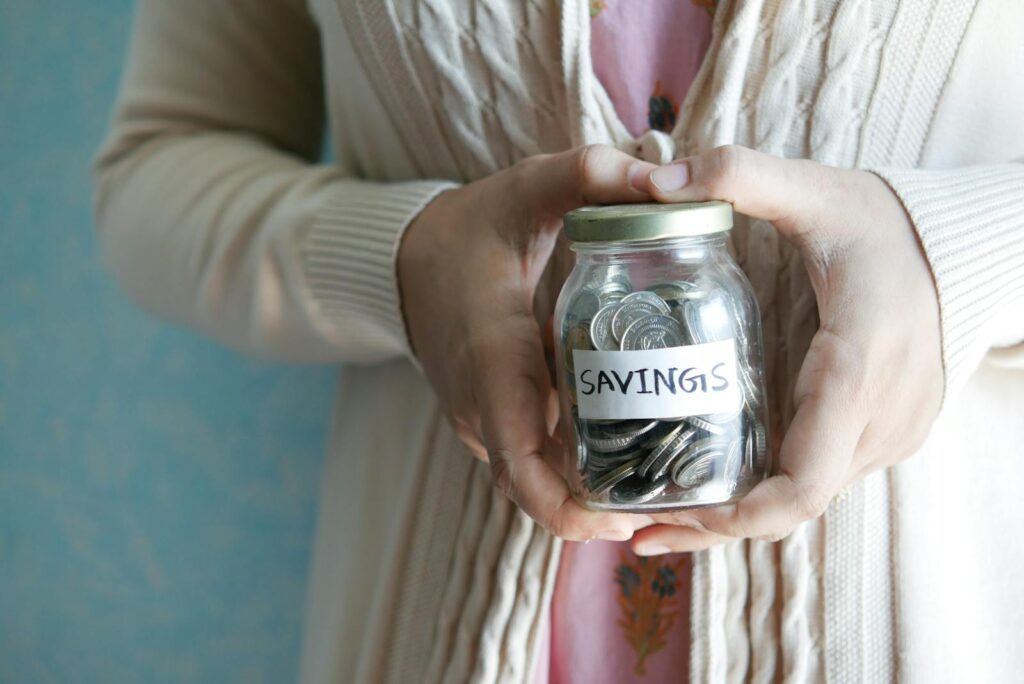 Woman holding a jar labeled 'savings' filled with coins, representing financial savings.