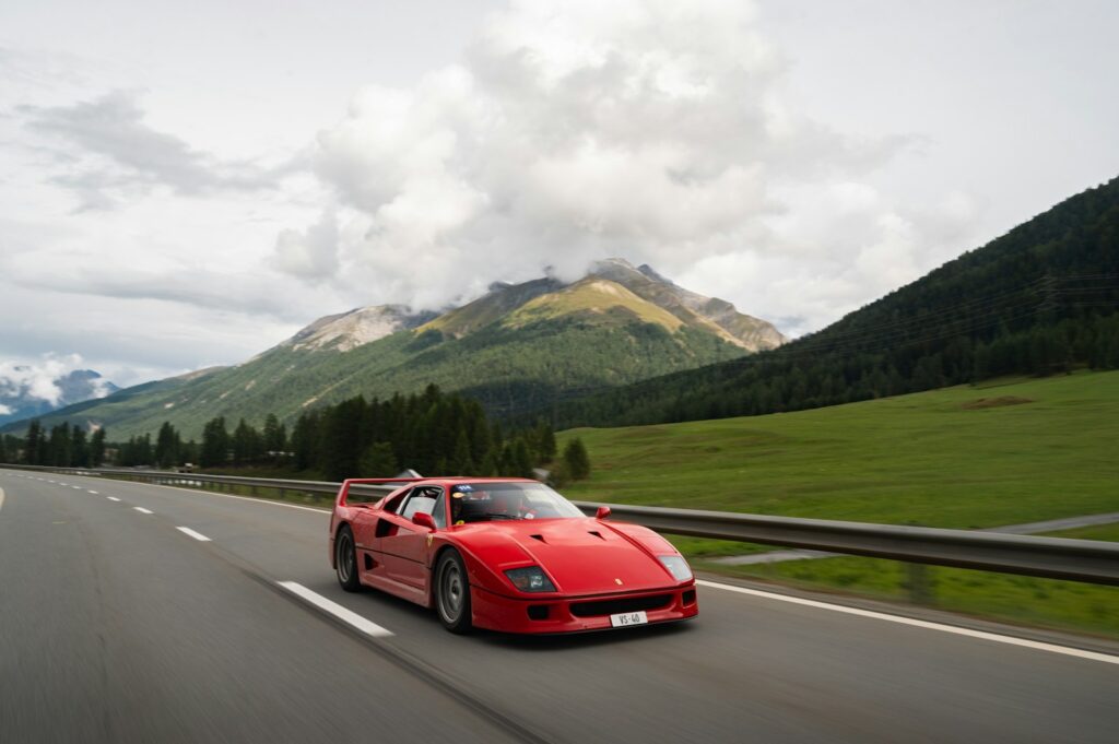a red sports car driving on a road with mountains in the background