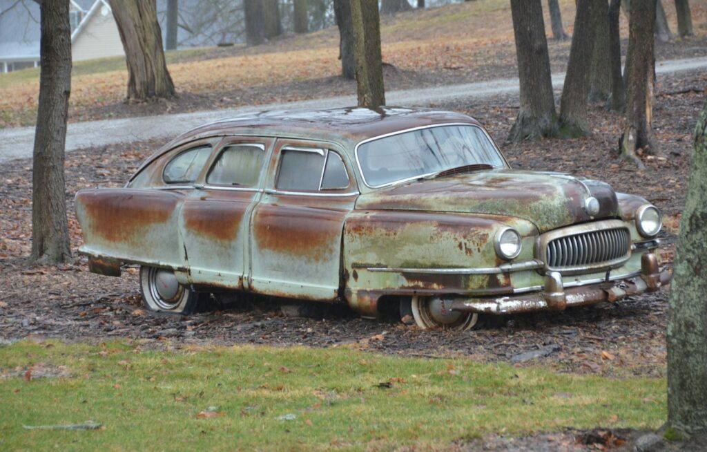 an old rusty car sitting in the middle of a forest