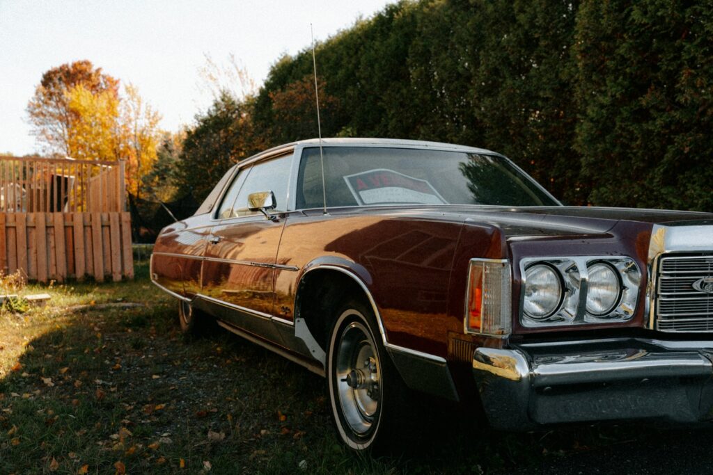 Vintage maroon car parked outdoors near trees.