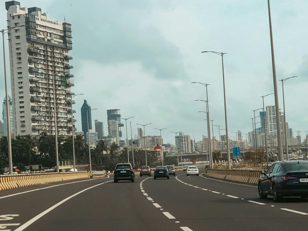 Cars drive on a city highway with tall buildings.