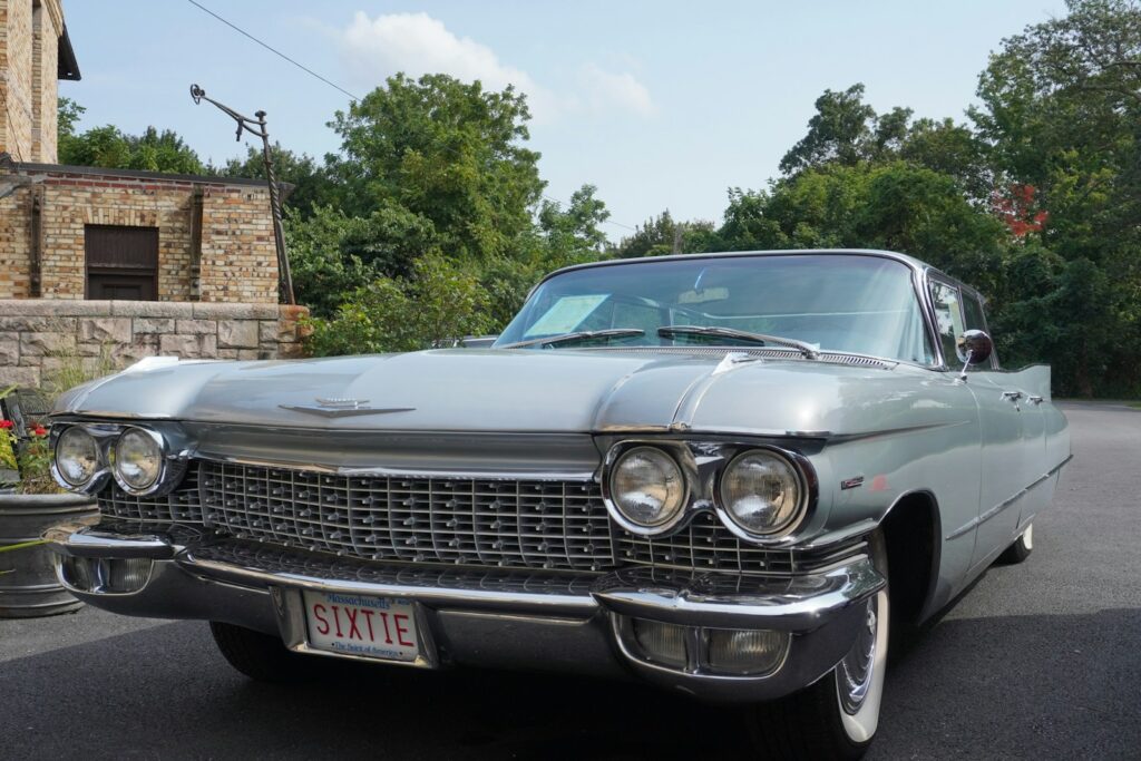 A vintage silver cadillac parked outdoors near a brick building.