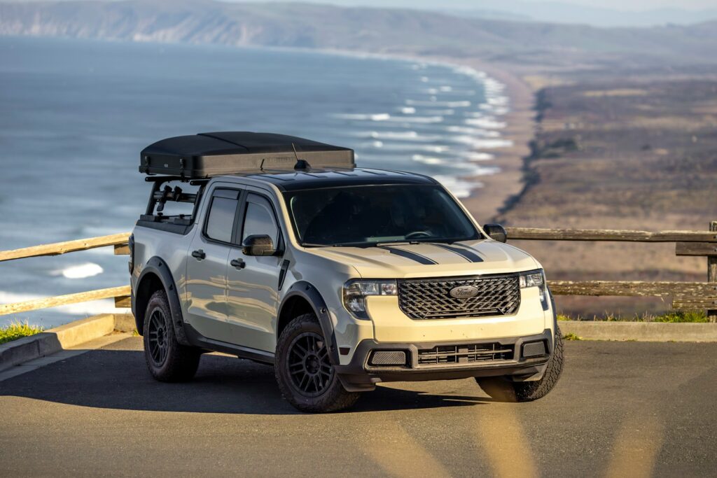Tan pickup truck with rooftop tent parked overlooking ocean
