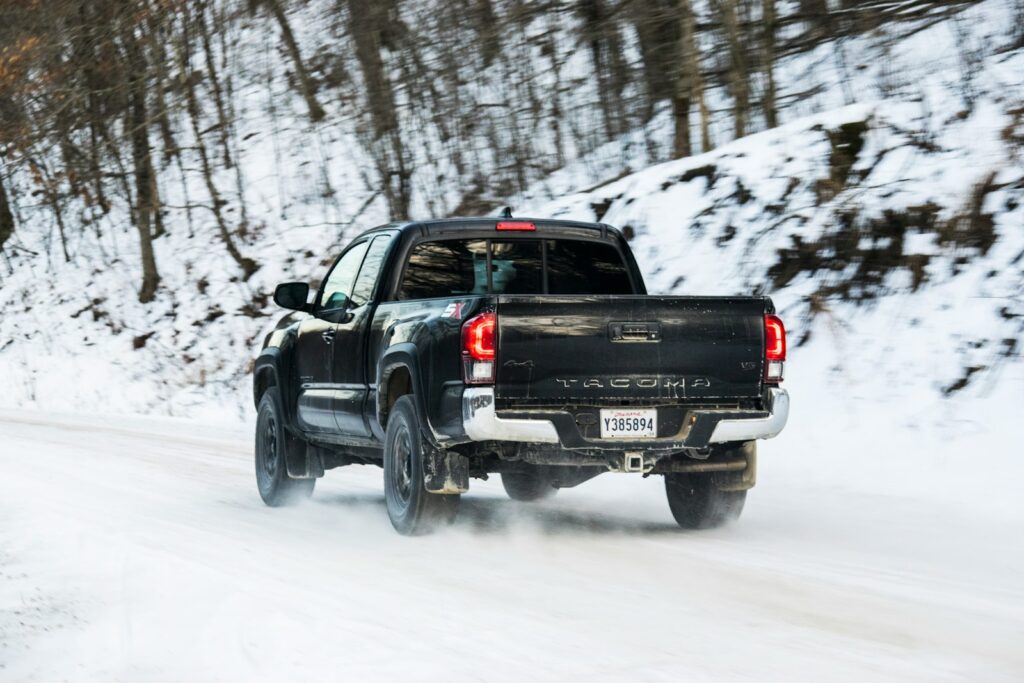 A black truck drives on a snowy road.