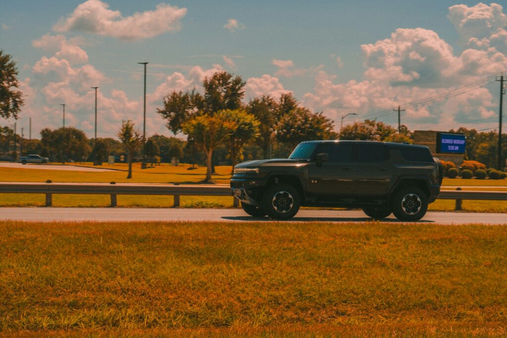 Dark suv drives along a grassy roadside.