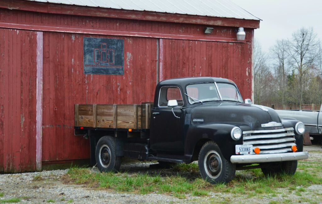 A black truck is parked next to a red barn.