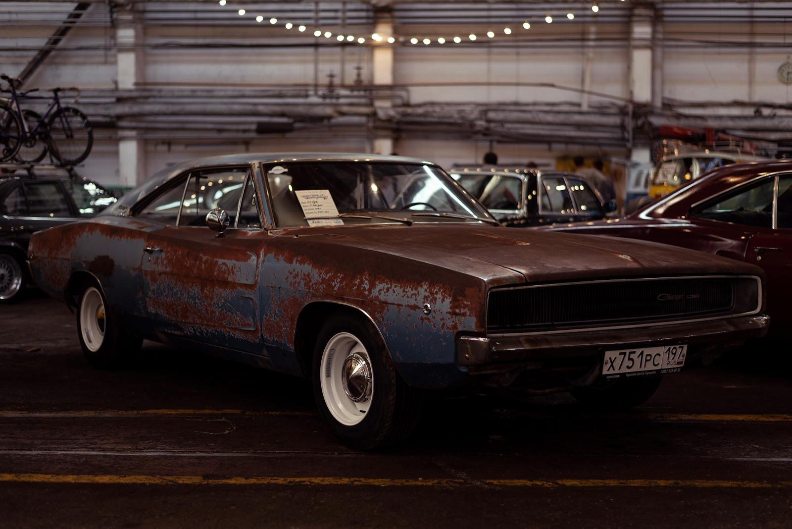 A rusty classic Dodge Charger on display at an indoor car show, showcasing its vintage charm.