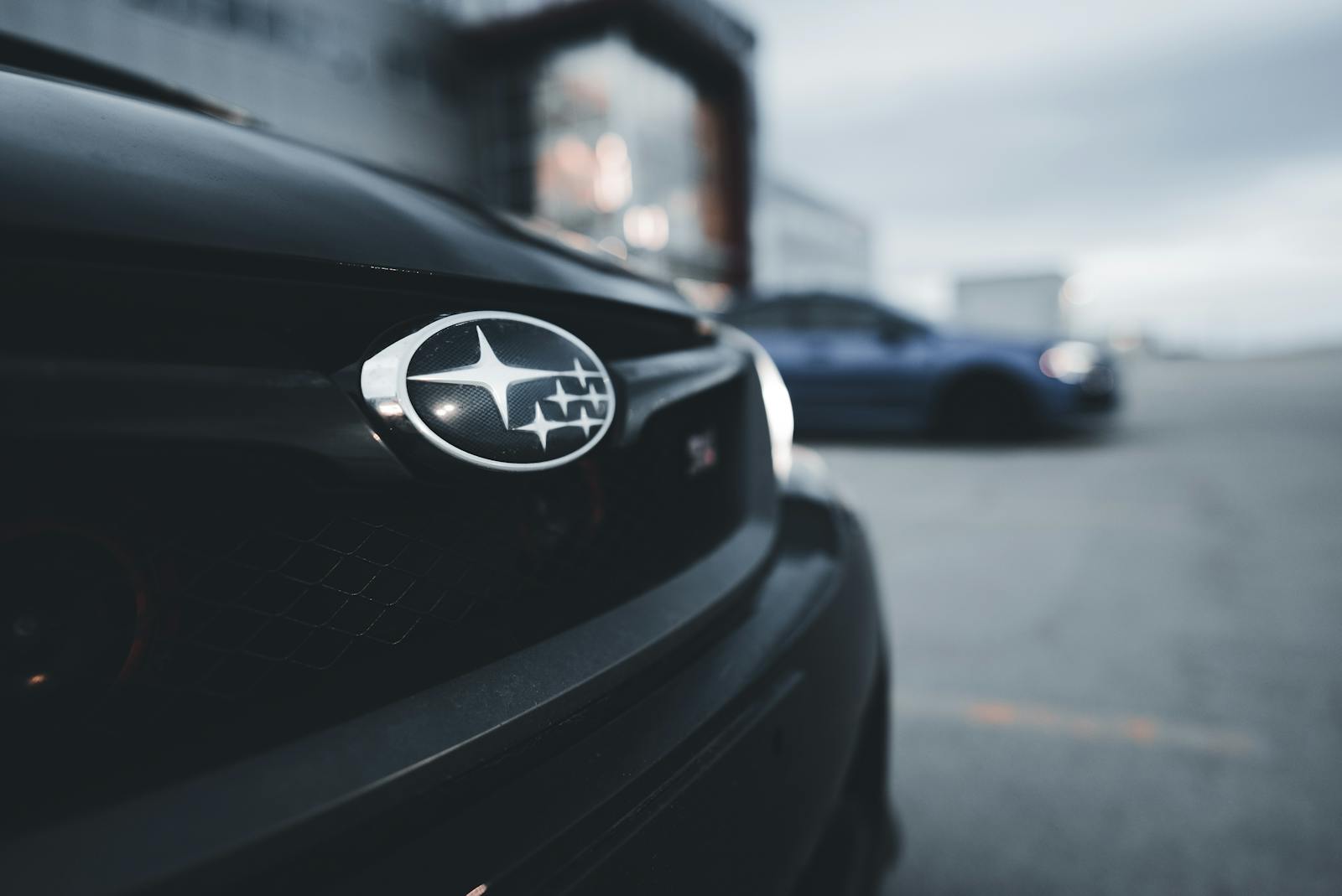 Detail of a Subaru WRX grille with an out-of-focus background featuring another car.
