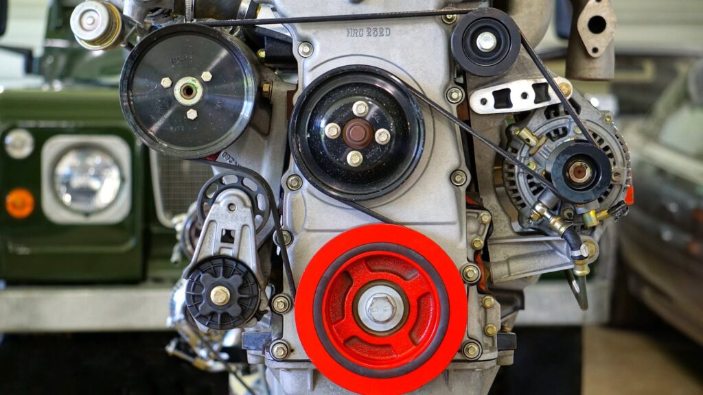 Detailed view of a car engine showcasing belts and colorful pulleys in a workshop setting.