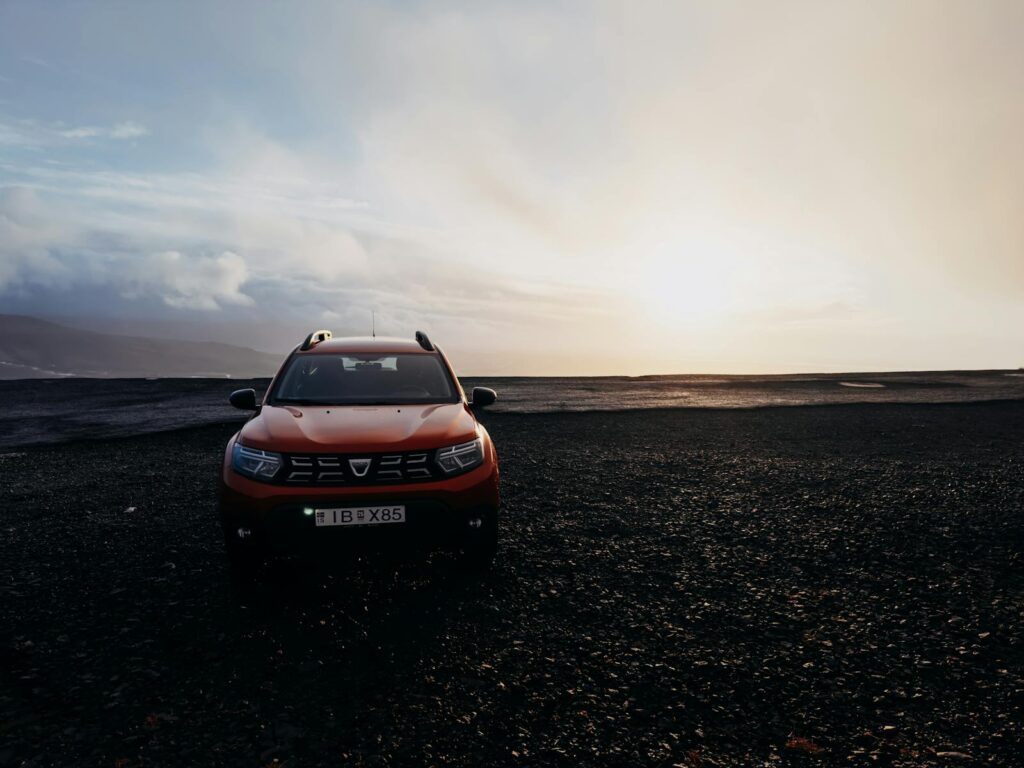 A red SUV parked on a rocky landscape under a dramatic sunrise, showcasing offroad capability.