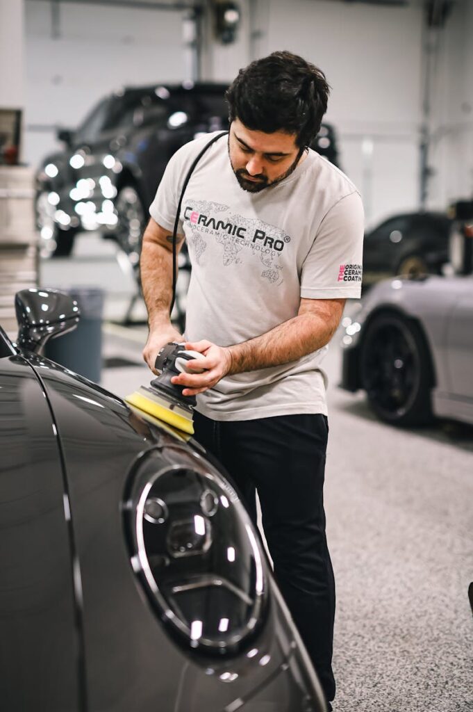 A man carefully polishes a sleek sports car in a professional auto detailing garage.
