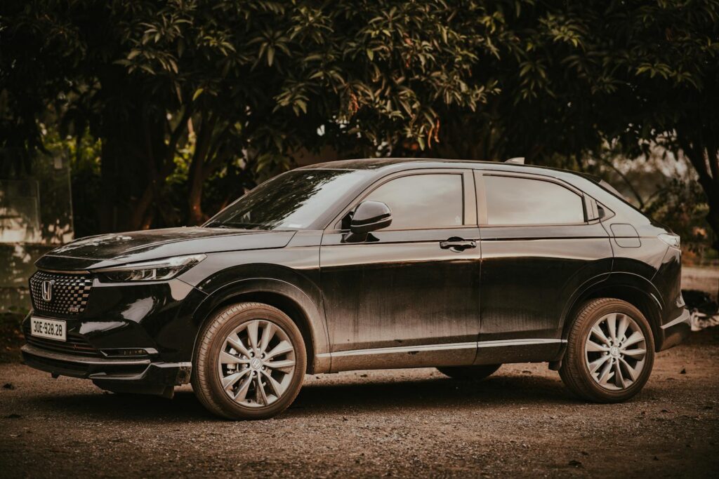 A stylish black Honda HR-V SUV parked outdoors amongst trees on a sunny day.