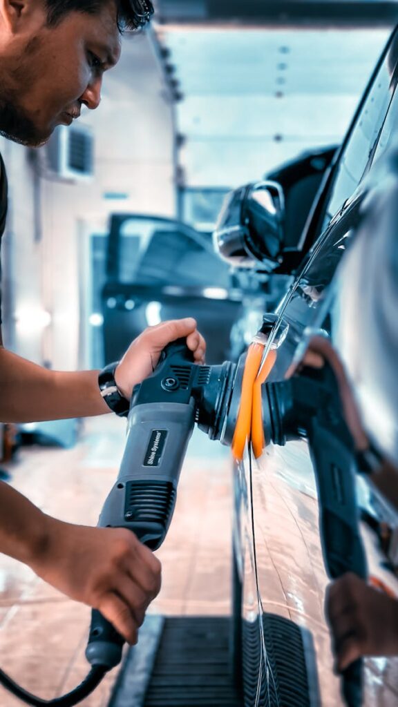 Close-up of a man polishing a car in a garage using an electric buffer tool, showcasing car maintenance.