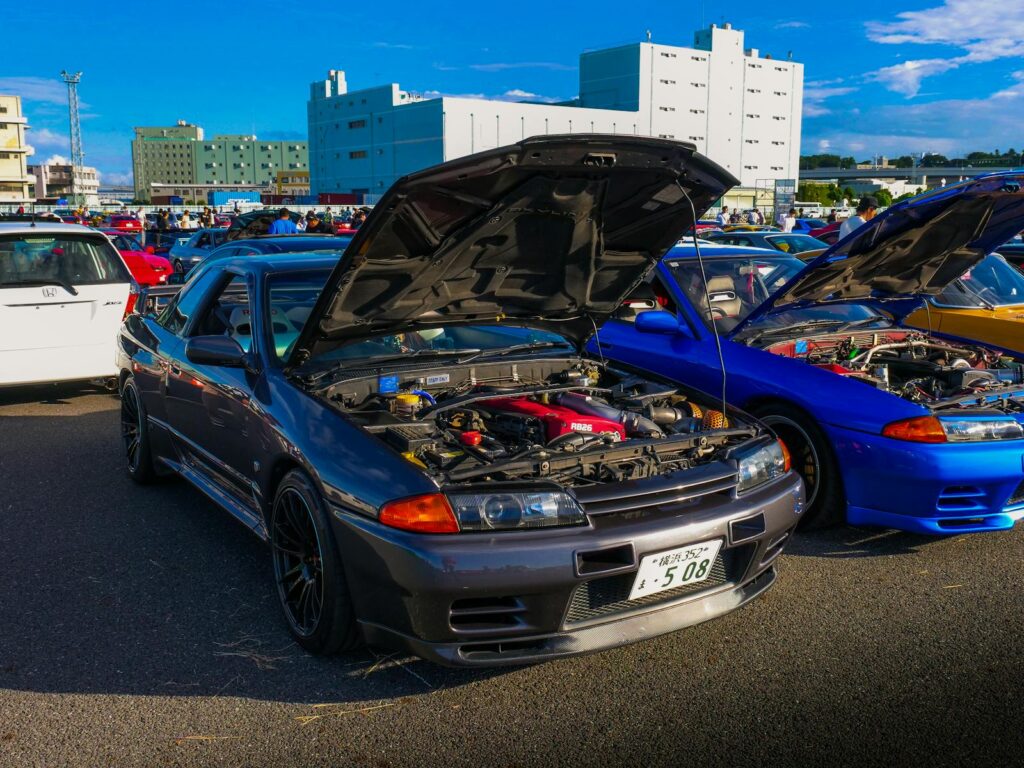 A collection of classic JDM cars with open hoods at an outdoor car meet, showcasing iconic Japanese vehicle culture.