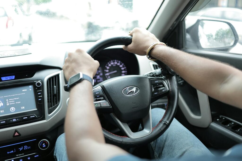 Close-up of a person driving a Hyundai car, showcasing hands on the steering wheel and dashboard detail.