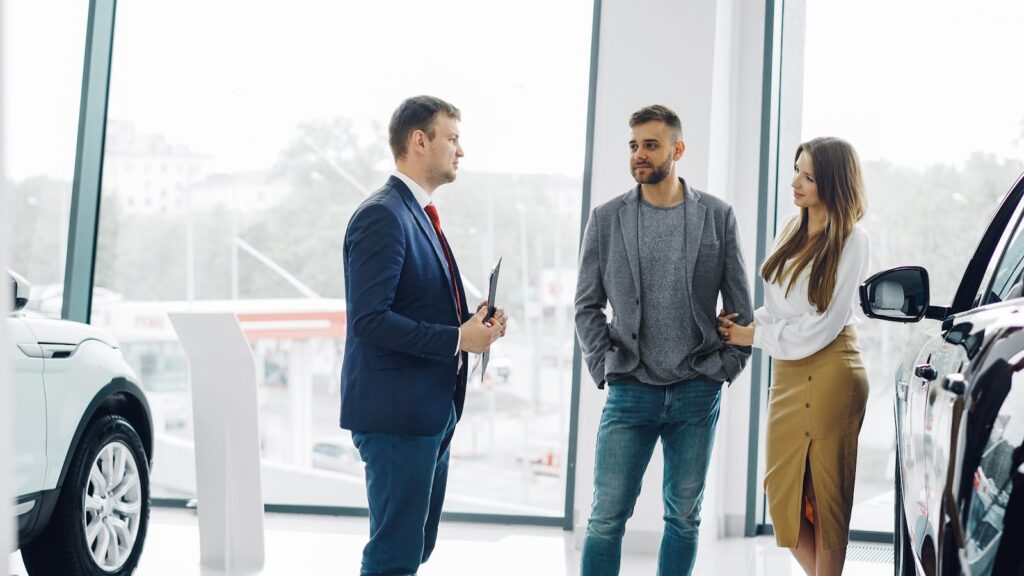 Business professional consulting a couple in a modern car dealership setting.