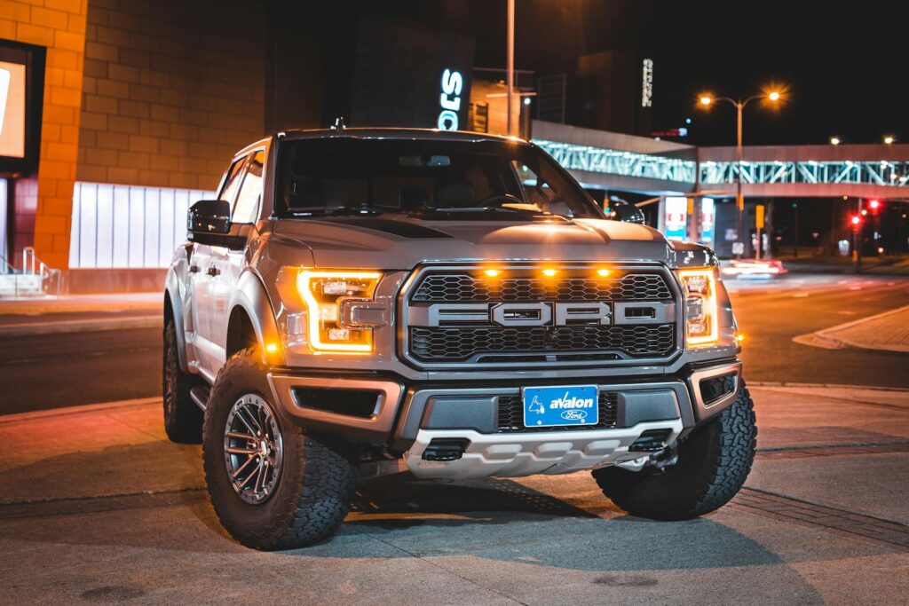 A Ford truck with illuminated headlights parked on a quiet urban street at night.