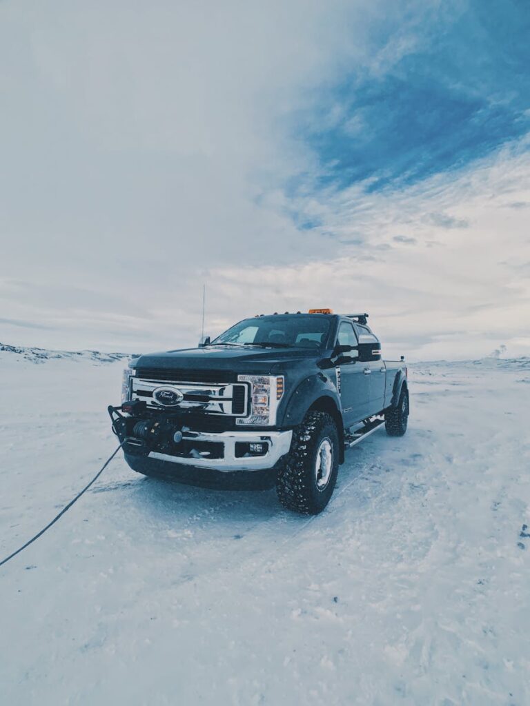 Modern black vehicle driving on trailer on snowy ground against cloudy sky in winter time in daylight in cold weather