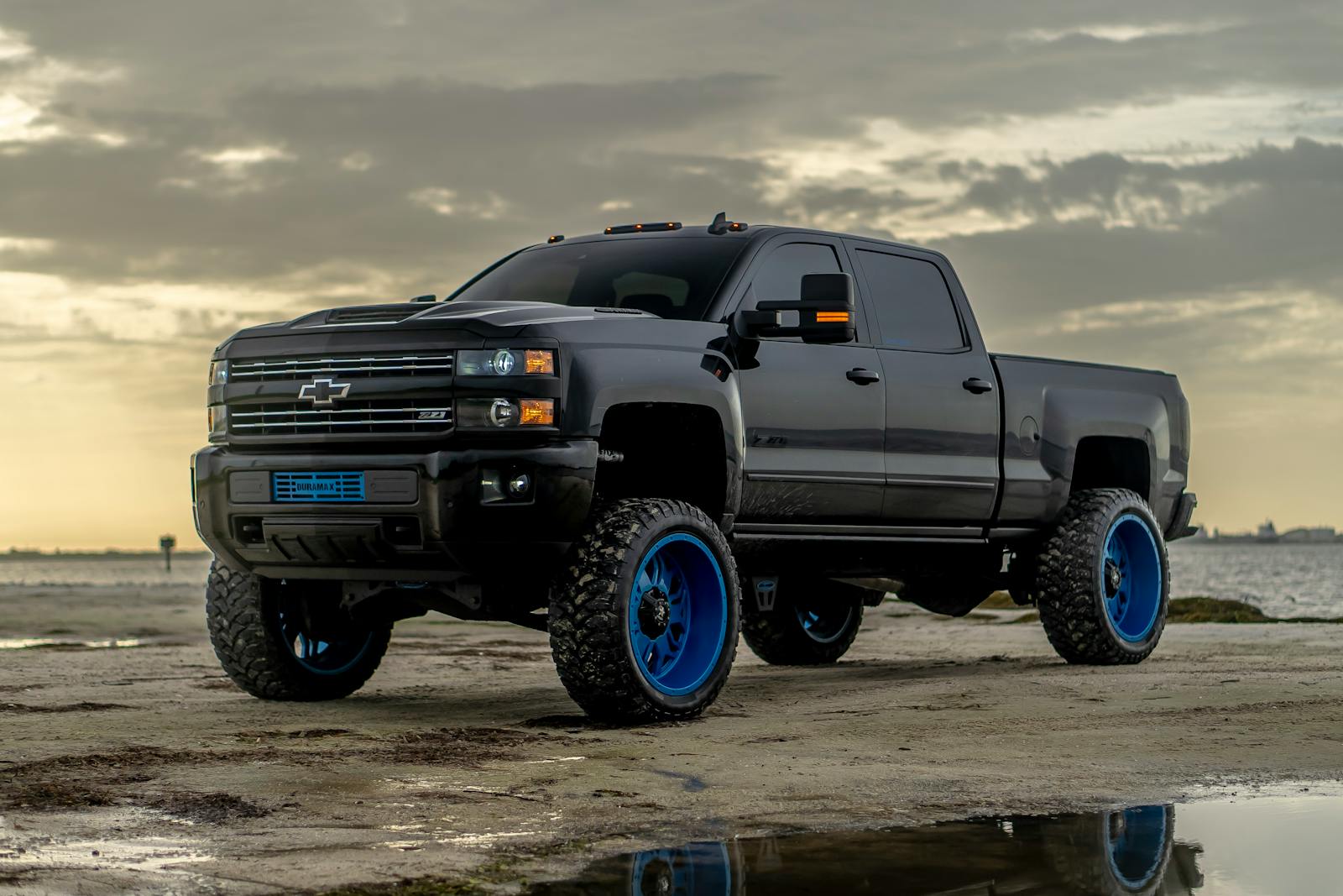 A black custom pickup truck with striking blue wheels parked on a sandy beach at dawn.