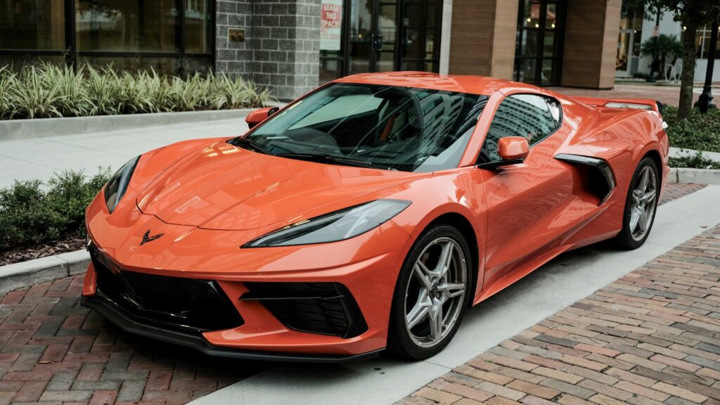High-quality image of a shiny orange Corvette sports car parked on a brick road.