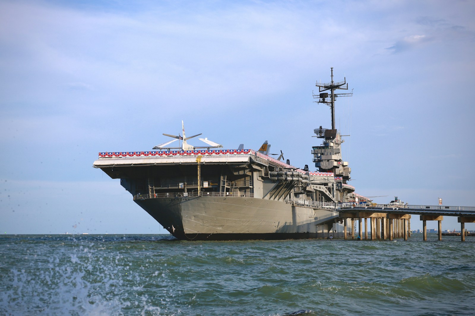 An aircraft carrier docked at a pier by the sea.