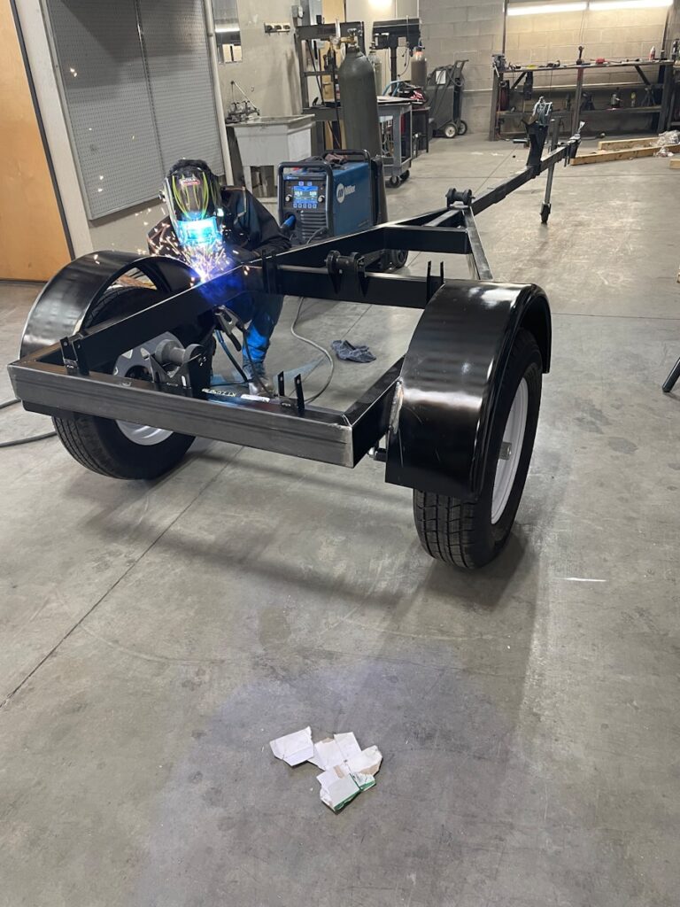 Welder working on a trailer frame in a workshop.