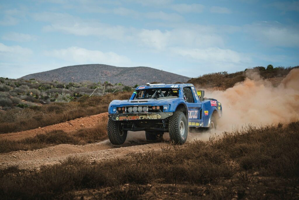 Blue off-road truck kicking up dust on a dirt track.