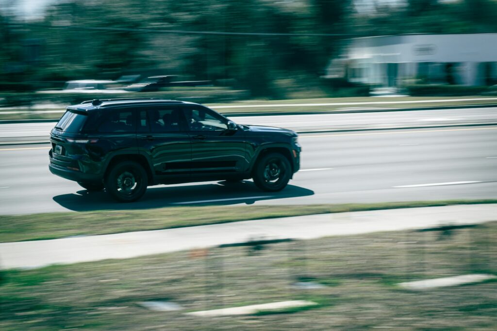 A dark suv drives down a blurred road.