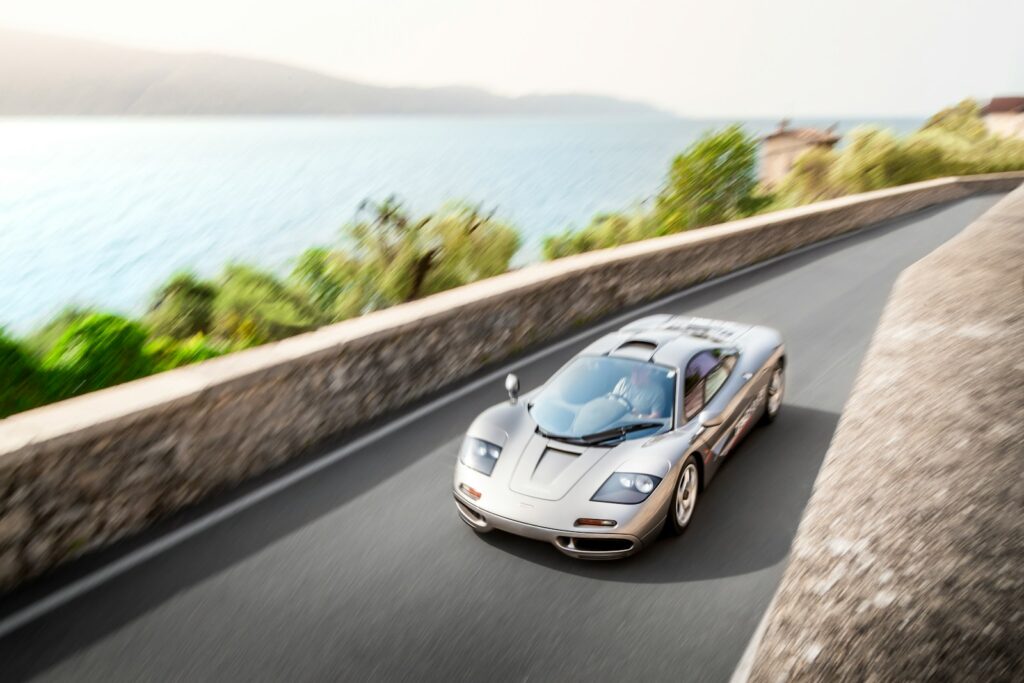 A white sports car driving down a road next to the ocean