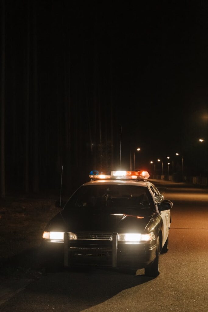 A solitary police car parked on a quiet, dark street at night with emergency lights flashing.