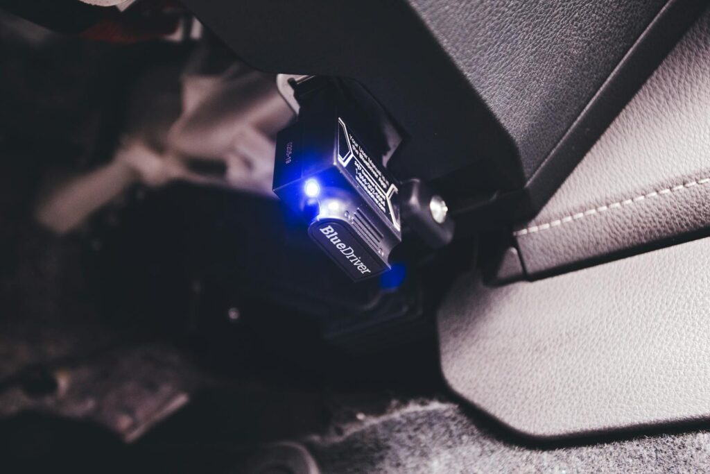 Close-up of a Bluetooth code reader tool connected inside a vehicle, illuminated by a blue light.