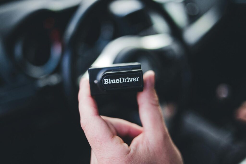 Detailed image of a hand holding a Bluedriver OBD2 scanner inside a car.