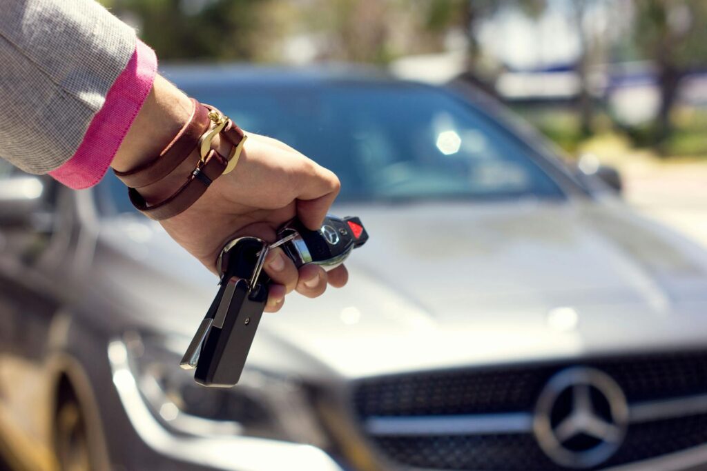 A close-up image of a hand holding car keys against the backdrop of a luxury car, outdoors.