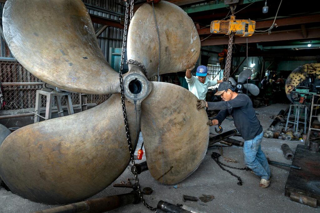 Two men working together to handle a massive industrial propeller in a workshop setting.