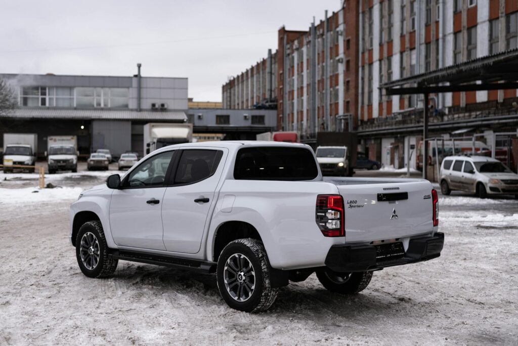 A white pickup truck parked in a city area with snow and urban buildings.