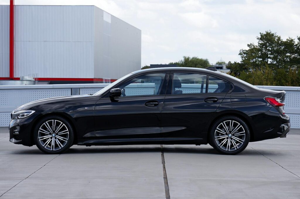 Side profile of an elegant black BMW sedan parked outdoors with modern architecture backdrop.