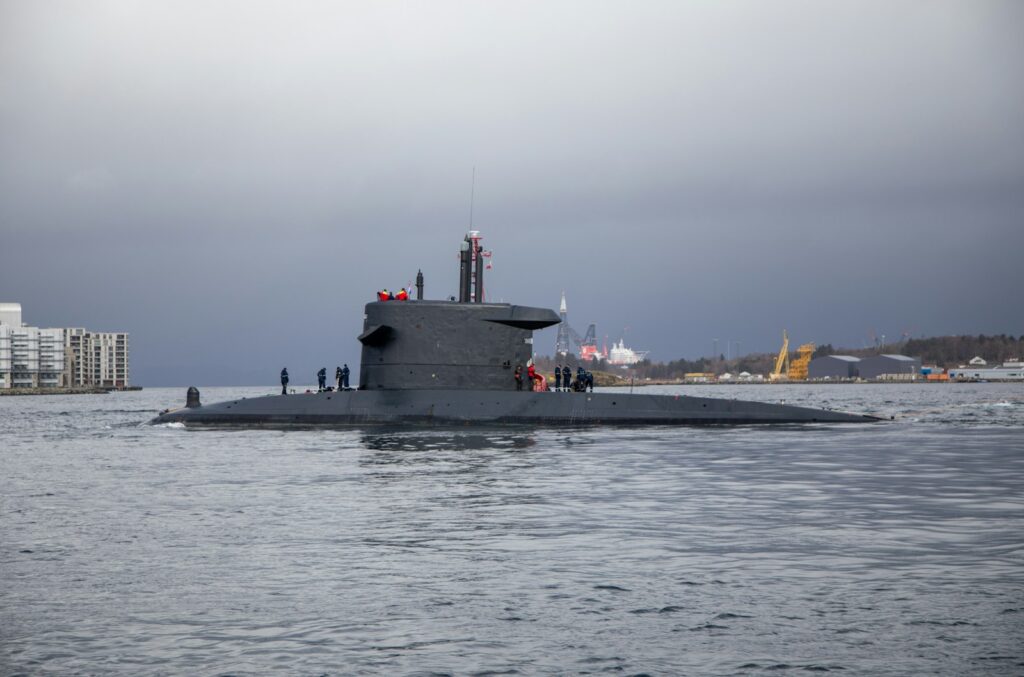 A submarine sails on the water with people on deck.
