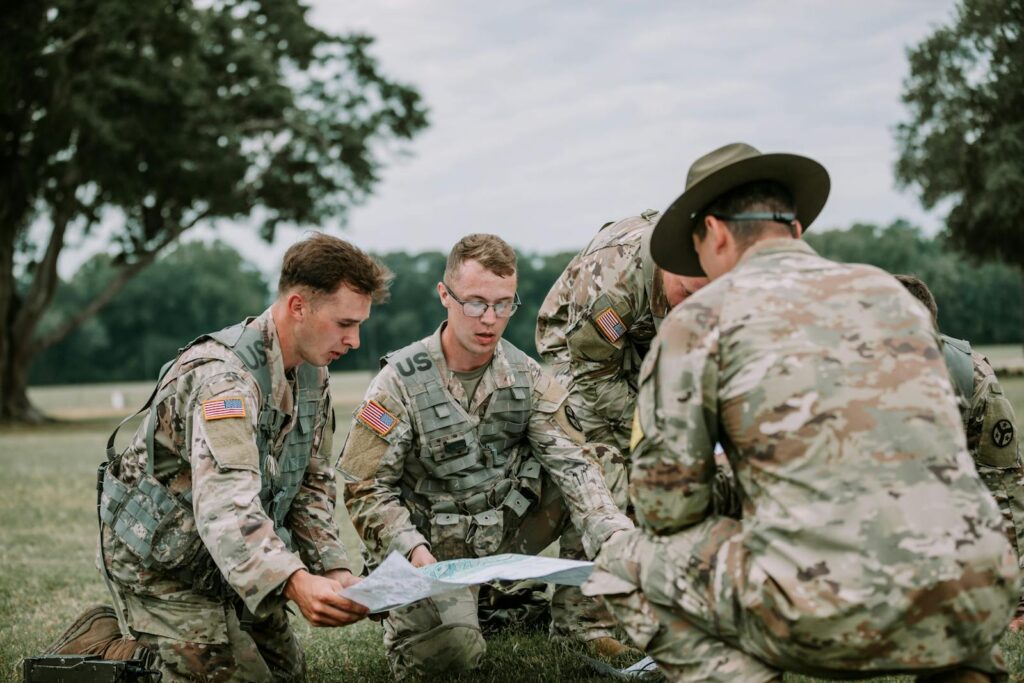 U.S. soldiers in camo gear analyze a map at Fort Moore, GA during drill.