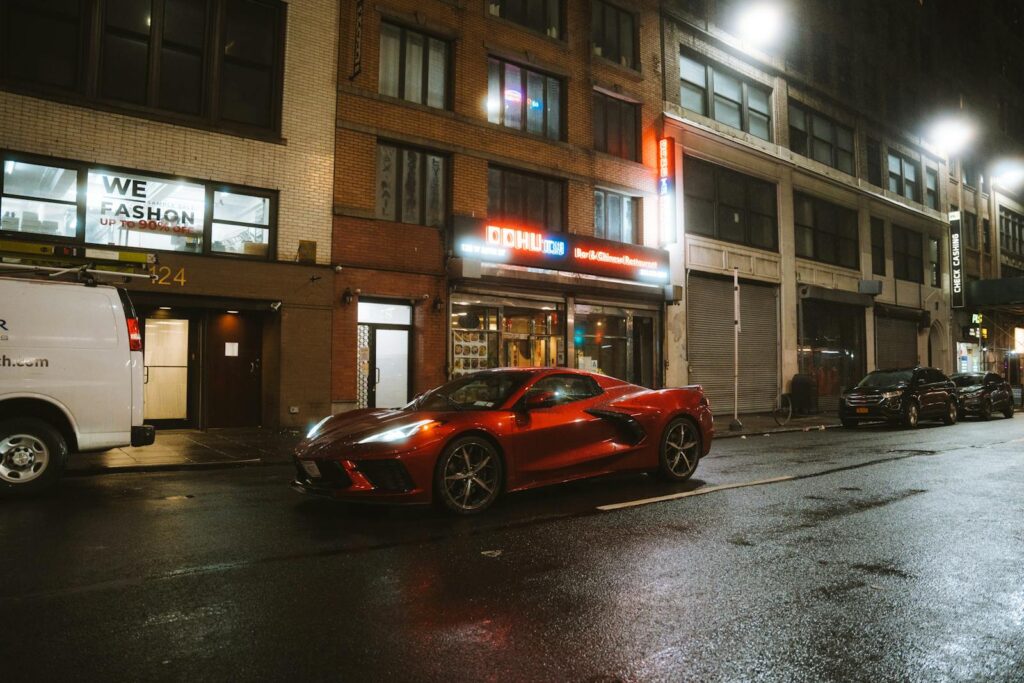 A sleek red sports car, possibly a Chevrolet Corvette, parked on a bustling city street at night.