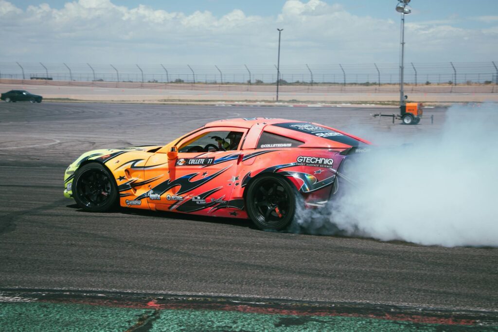 Vibrant Chevrolet Corvette drifting on a track, creating billowing smoke against a clear sky.