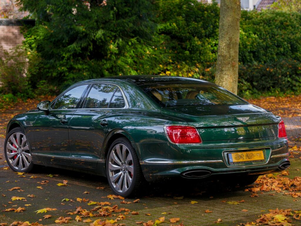 Green Bentley car parked on a leaf-strewn road, showcasing luxury and elegance.