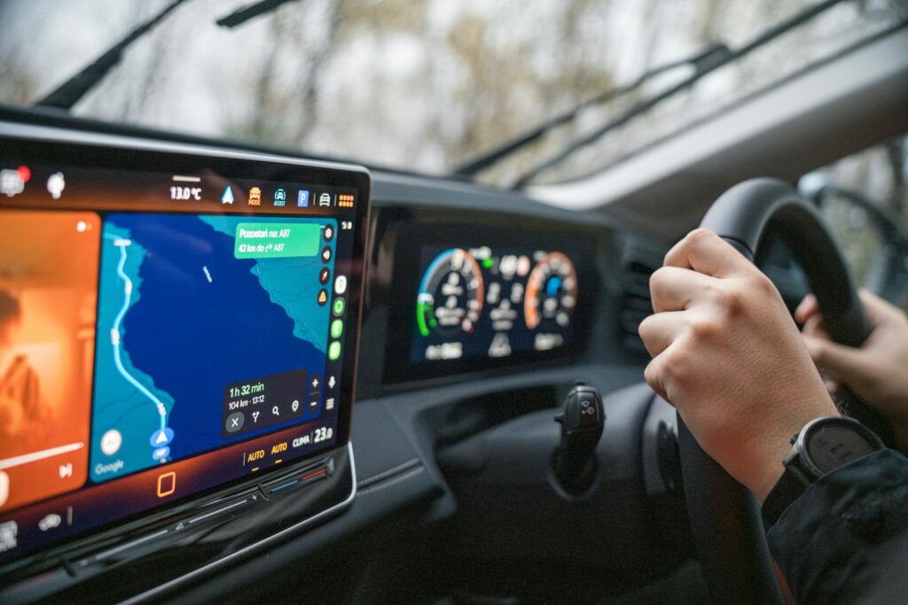 Close-up of hands on steering wheel and GPS navigation on car dashboard, showcasing modern driving technology.