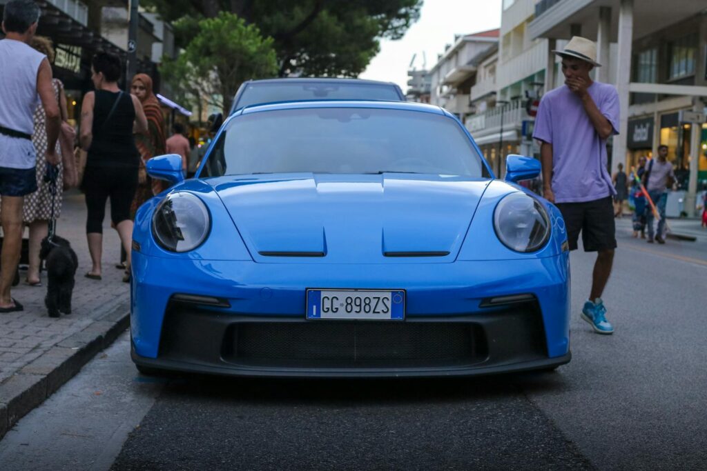 Vibrant blue sports car parked in bustling city street with pedestrians.