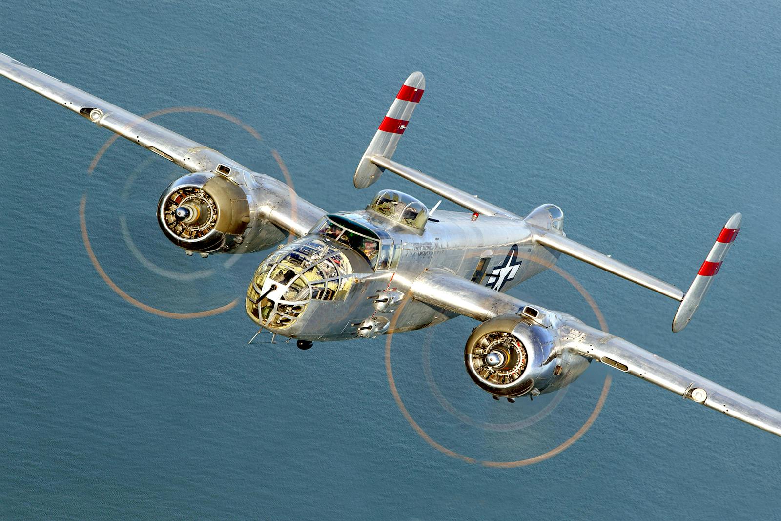 Historic B-25 Mitchell bomber flying over the ocean in clear skies.