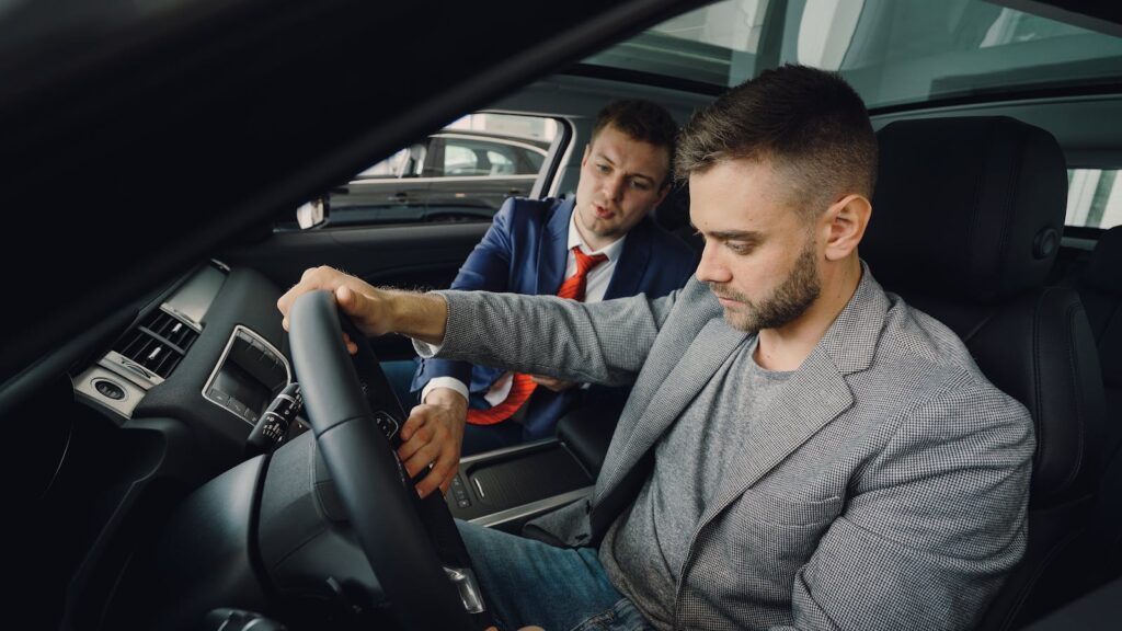 Salesman demonstrating car features to potential buyer inside vehicle showroom.