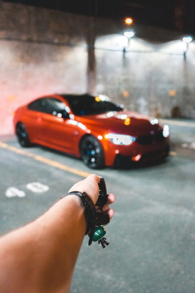 Crop hand of anonymous person using remote key to open red sport car on grunge parking