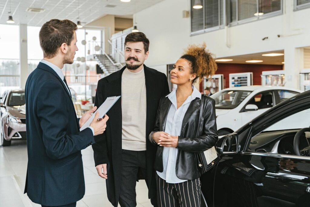 Couple discussing car purchase with salesman at indoor dealership, engaging conversation.