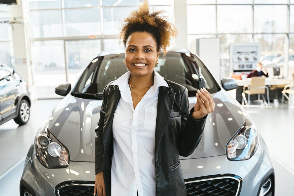 Smiling woman holding car keys in a dealership showroom, celebrating her new car purchase.