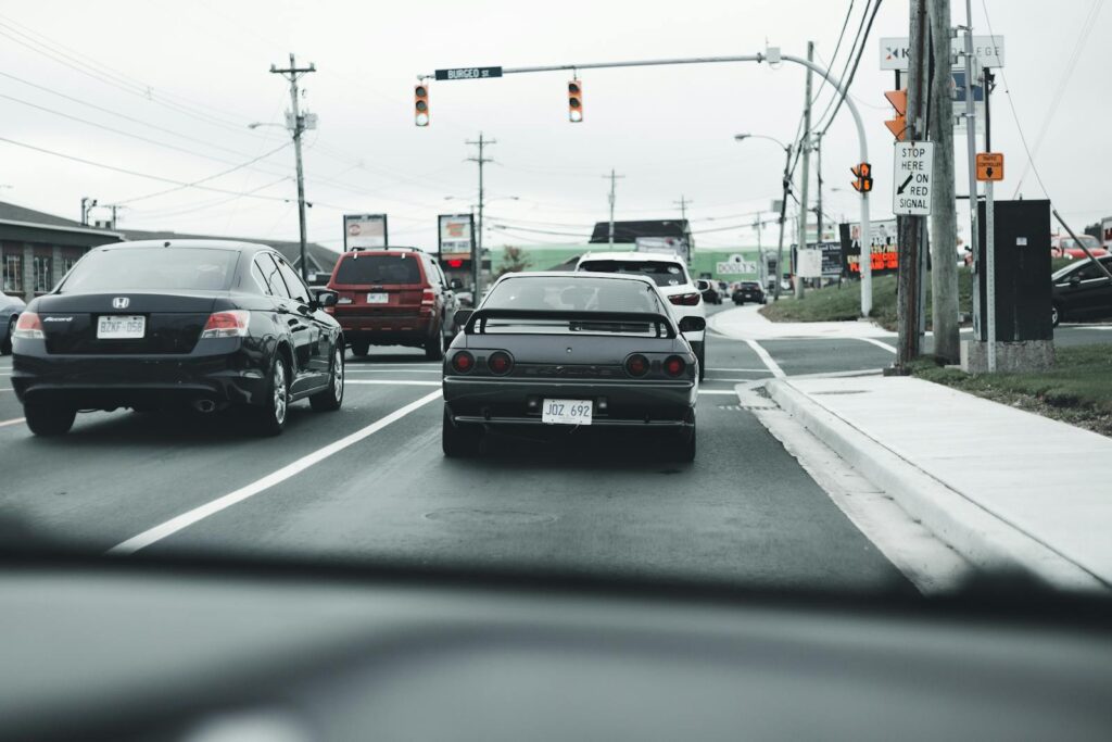 A busy road traffic scene with multiple cars and stop lights under cloudy skies.